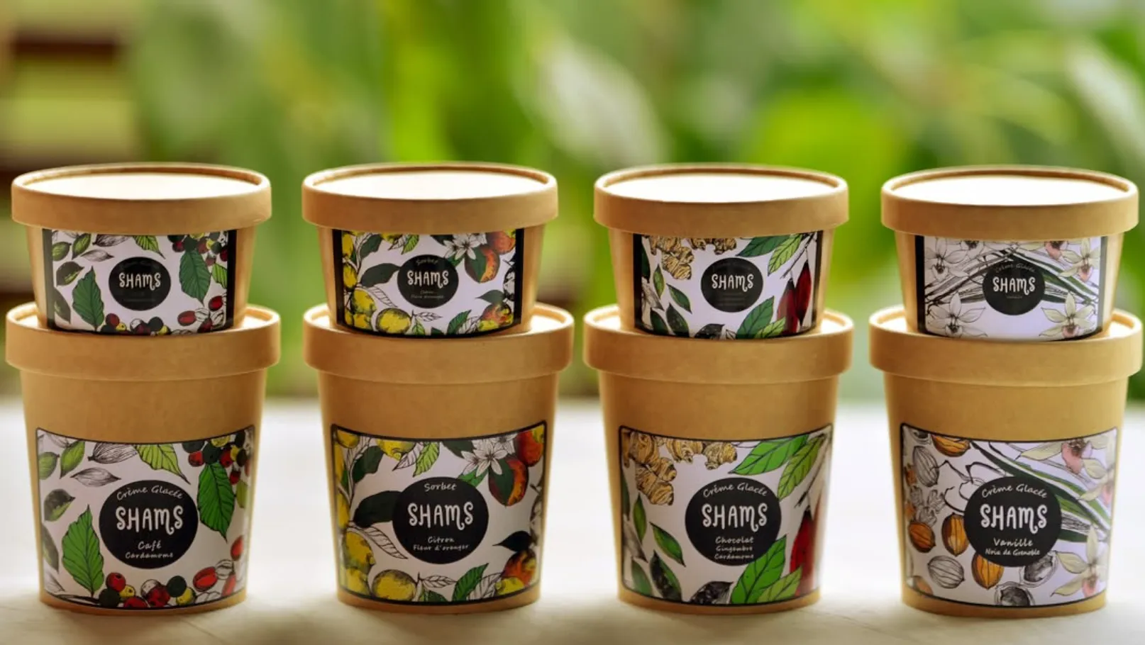 Huit pintes Shams empilées dans un jardin — Café Cardamome, Créponné citron fleur d’oranger, Chocolat cardamome gingembre, Vanille Noix de Grenoble
